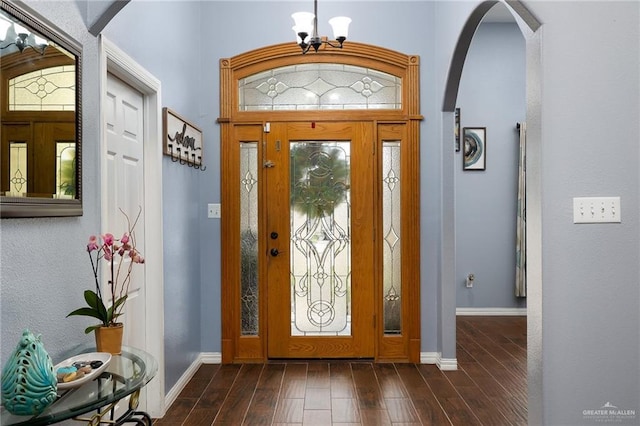 entryway with dark wood-type flooring, arched walkways, baseboards, and an inviting chandelier