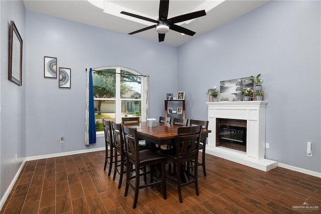 dining area with ceiling fan, baseboards, wood finished floors, and a glass covered fireplace