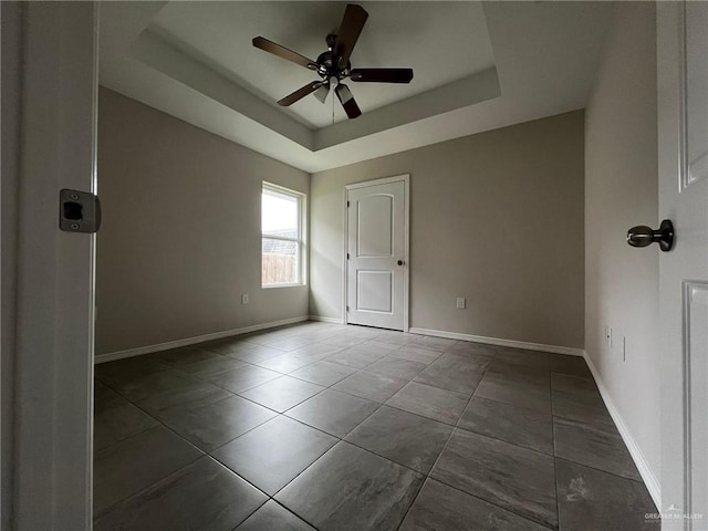 tiled empty room featuring a tray ceiling and ceiling fan