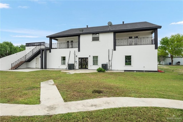 back of property with a balcony, central air condition unit, and a yard