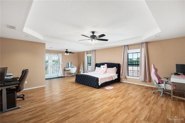 bedroom with ceiling fan, multiple windows, light wood-type flooring, and a tray ceiling