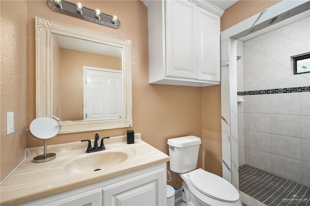 bathroom with toilet, a tile shower, and vanity