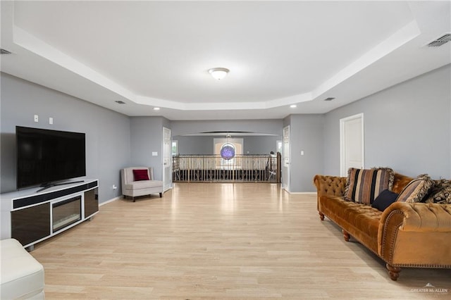 living room with a raised ceiling and light wood-type flooring