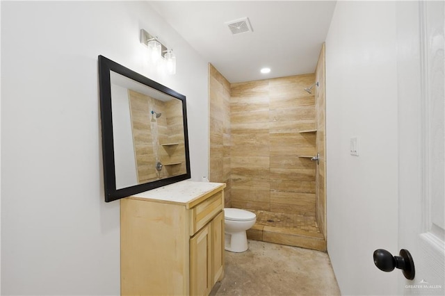 bathroom with tiled shower, vanity, toilet, and concrete flooring