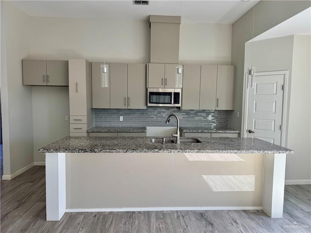 8706 Pink Flamingo St, Harlingen, TX 78552 - kitchen featuring a sink, stainless steel microwave, baseboards, decorative backsplash, and light wood-style flooring