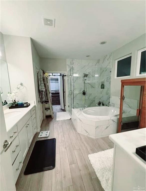 bathroom featuring a garden tub, a marble finish shower, visible vents, vanity, and wood finished floors