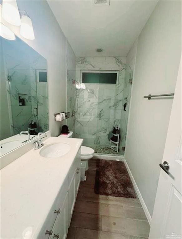 bathroom featuring toilet, wood finish floors, vanity, baseboards, and a marble finish shower