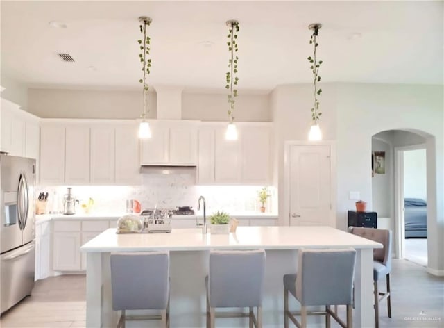 kitchen with hanging light fixtures, white cabinetry, a center island with sink, and stainless steel refrigerator with ice dispenser