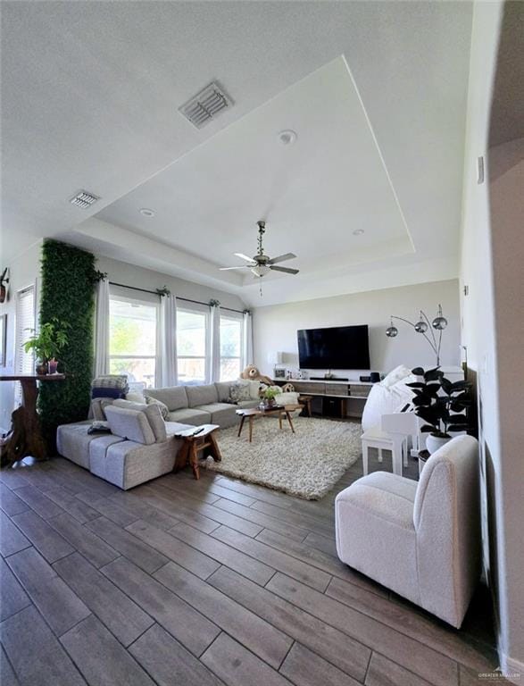 living room with wood finished floors, a raised ceiling, visible vents, and a ceiling fan