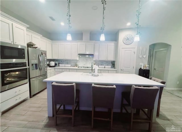 kitchen featuring arched walkways, stainless steel appliances, white cabinets, light countertops, and decorative backsplash