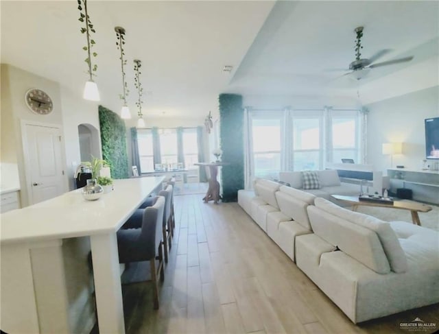 living room with arched walkways, ceiling fan, and light wood-style flooring