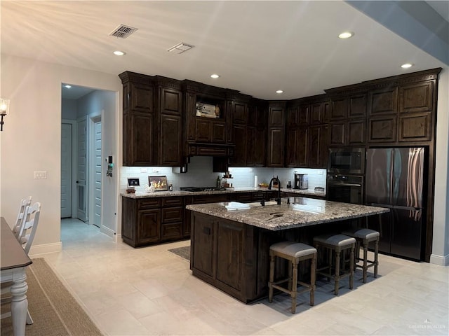 kitchen featuring a breakfast bar area, stone countertops, dark brown cabinets, appliances with stainless steel finishes, and a kitchen island with sink