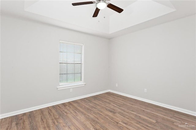 empty room featuring wood-type flooring, a tray ceiling, and ceiling fan