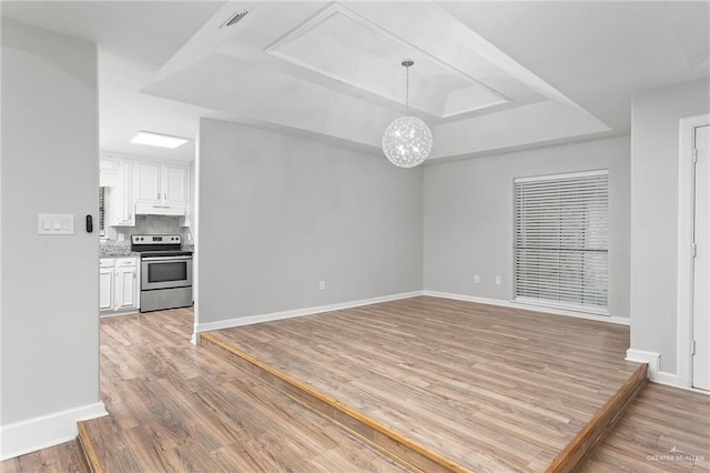 spare room featuring a tray ceiling, hardwood / wood-style floors, and a notable chandelier