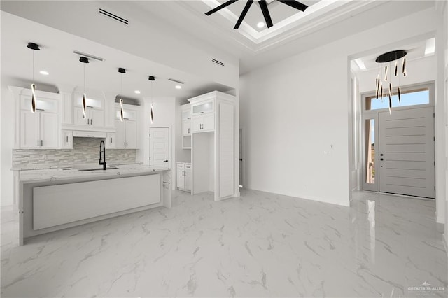 kitchen with light stone countertops, sink, backsplash, decorative light fixtures, and white cabinets