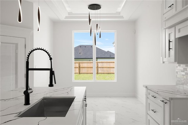 kitchen featuring light stone countertops, sink, a raised ceiling, pendant lighting, and white cabinets