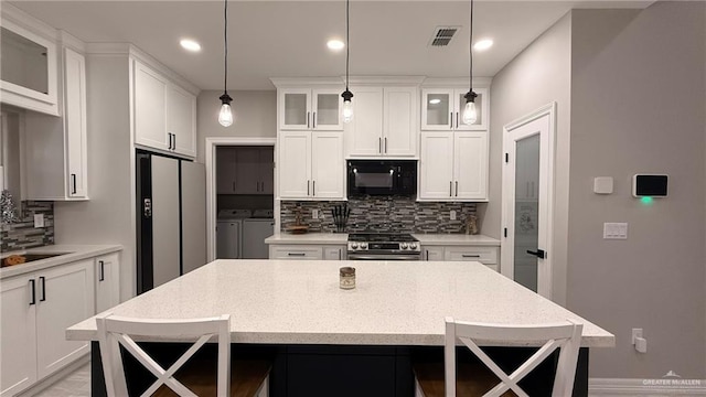 kitchen with washer and clothes dryer, pendant lighting, decorative backsplash, appliances with stainless steel finishes, and a breakfast bar area