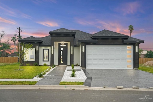 prairie-style home with a yard, roof with shingles, an attached garage, and driveway