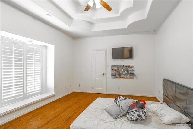 bedroom with ceiling fan, light hardwood / wood-style floors, and a raised ceiling