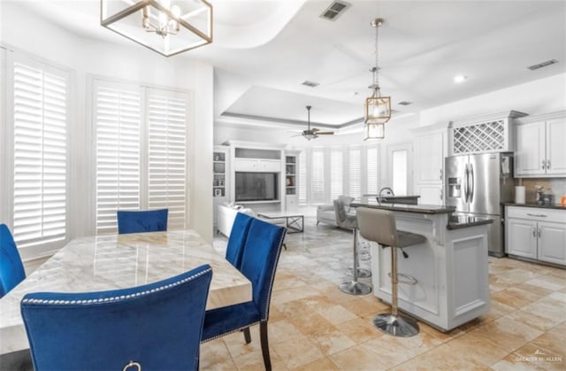 dining room with ceiling fan with notable chandelier and a raised ceiling