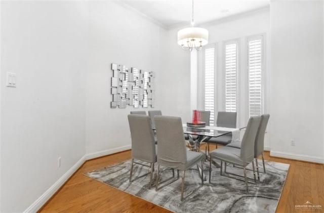 dining area with wood-type flooring, ornamental molding, and an inviting chandelier