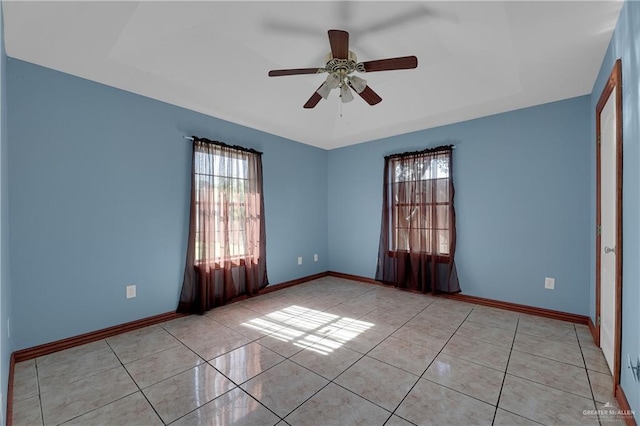 tiled empty room featuring a raised ceiling and ceiling fan