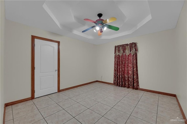 tiled empty room with a raised ceiling and ceiling fan