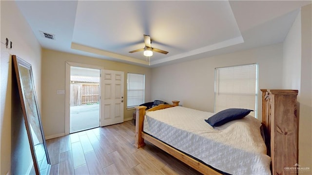 bedroom featuring access to exterior, light wood-type flooring, a raised ceiling, and ceiling fan