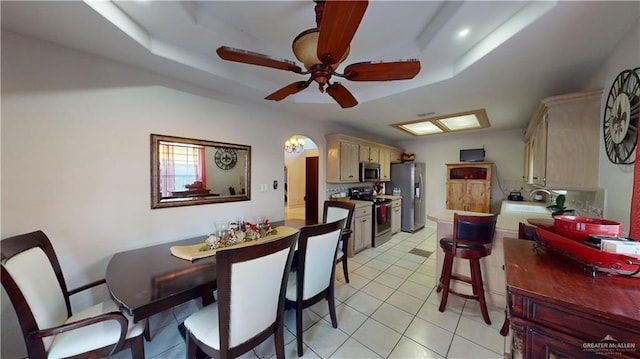 dining area featuring light tile patterned flooring, a tray ceiling, ceiling fan, and sink