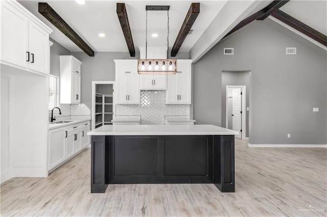 kitchen with backsplash, white cabinets, light wood-type flooring, beamed ceiling, and decorative light fixtures