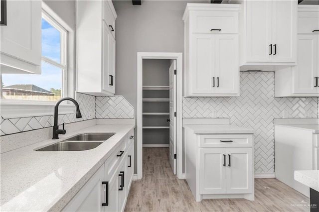 kitchen with white cabinets, light hardwood / wood-style floors, light stone countertops, and sink