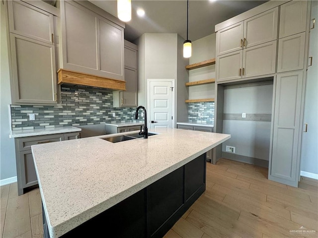 kitchen featuring light wood-type flooring, a sink, a kitchen island with sink, and decorative backsplash