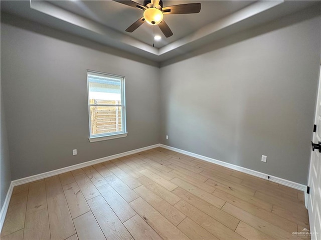 empty room with a ceiling fan, baseboards, a tray ceiling, and wood finished floors