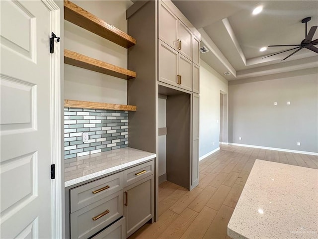 kitchen with a ceiling fan, light wood-style flooring, a tray ceiling, gray cabinets, and open shelves