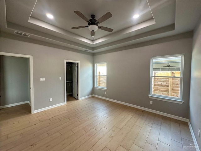 unfurnished bedroom with a tray ceiling, visible vents, a spacious closet, and wood finished floors