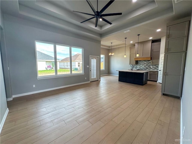 kitchen featuring light wood-style flooring, open floor plan, a tray ceiling, light countertops, and backsplash