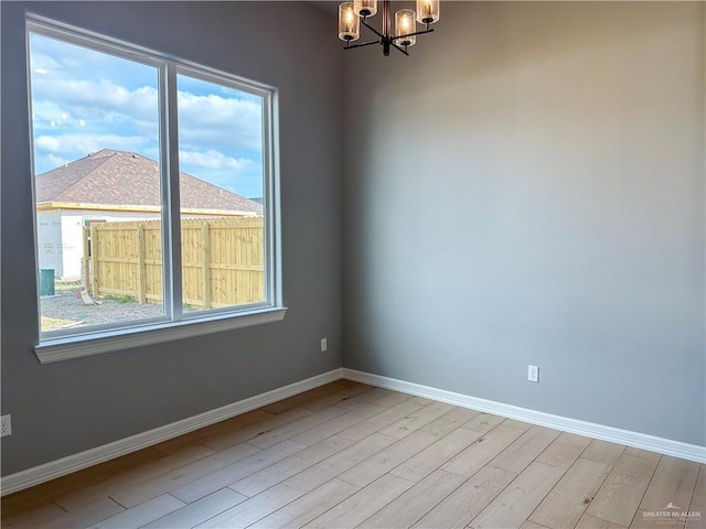 empty room featuring baseboards, light wood-style flooring, and an inviting chandelier