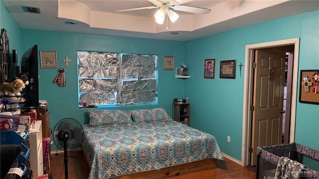 bedroom with hardwood / wood-style floors, a raised ceiling, and ceiling fan