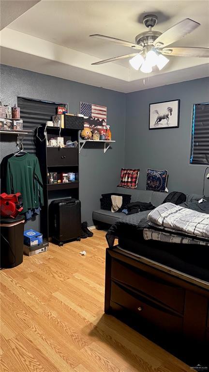 bedroom featuring ceiling fan, a raised ceiling, and wood-type flooring