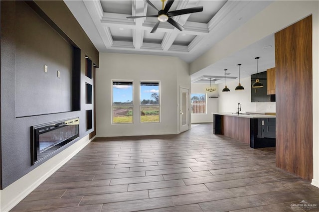 kitchen featuring beam ceiling, sink, hanging light fixtures, coffered ceiling, and an island with sink