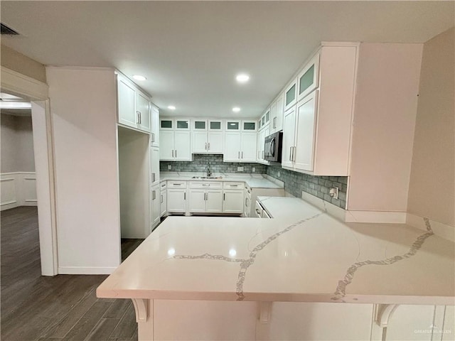 kitchen featuring dark hardwood / wood-style floors, decorative backsplash, light stone counters, kitchen peninsula, and a breakfast bar area