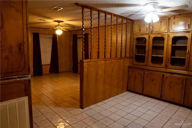 kitchen with light tile patterned flooring, ceiling fan, wood walls, and a textured ceiling