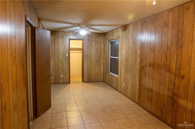 unfurnished room with light tile patterned floors, ceiling fan, wood walls, and a textured ceiling