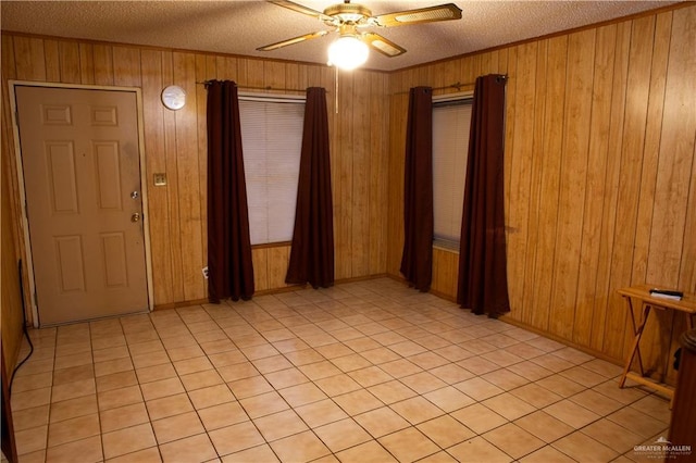 empty room with crown molding, ceiling fan, wood walls, and a textured ceiling