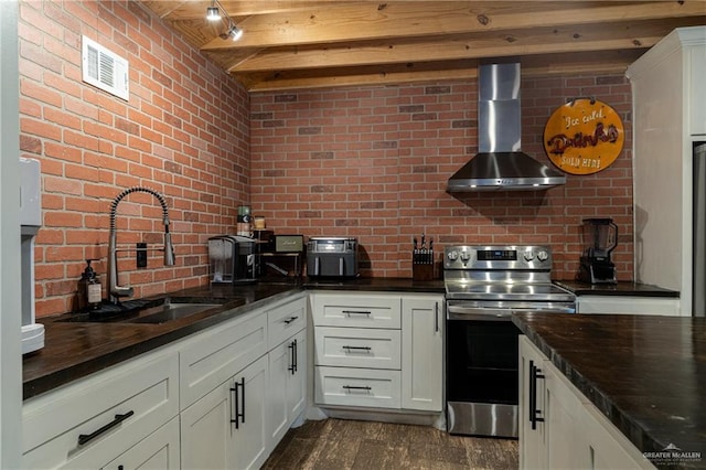 kitchen with dark wood finished floors, white cabinets, stainless steel range with electric cooktop, a sink, and wall chimney exhaust hood