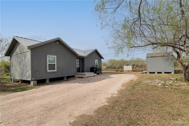 exterior space with dirt driveway, metal roof, a storage unit, and an outbuilding