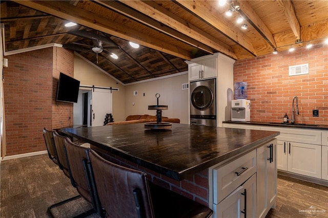 kitchen with a barn door, dark countertops, dark wood-style floors, stacked washing maching and dryer, and a sink