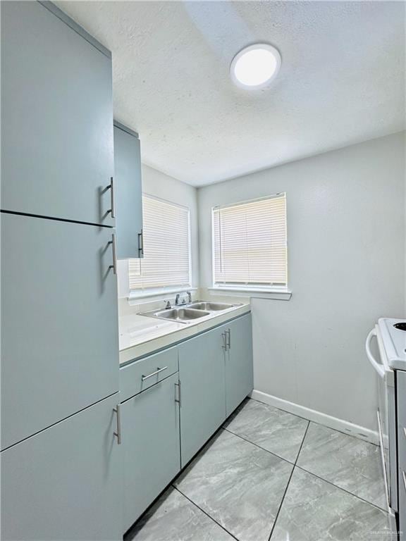 kitchen featuring light countertops, a sink, a textured ceiling, range, and baseboards