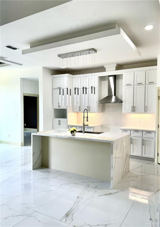 kitchen with wall chimney exhaust hood, sink, white cabinets, a kitchen island, and hanging light fixtures