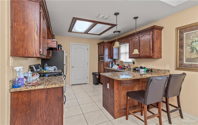 kitchen with kitchen peninsula, a kitchen bar, appliances with stainless steel finishes, pendant lighting, and light tile patterned flooring